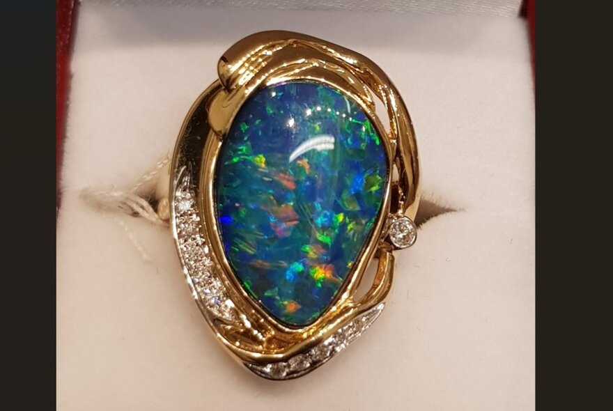 Teadrop-shaped blue and green opal pendant fringed with diamonds in a gold setting.