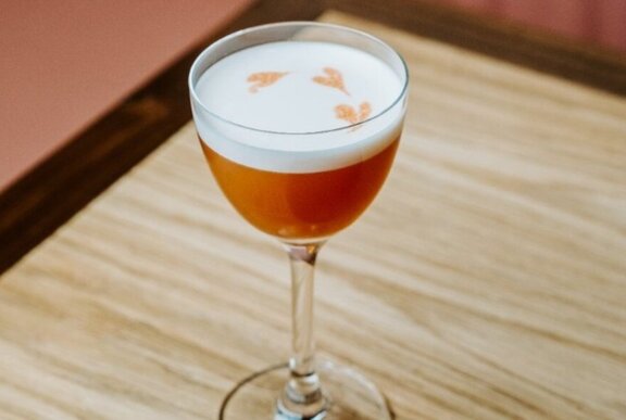 An espresso cocktail with a creamy white layer with three golden hearts in it.