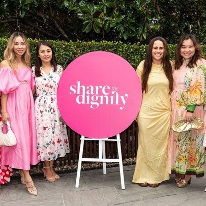 A pink 'Share the Dignity' sign with three women standing either side in dresses.