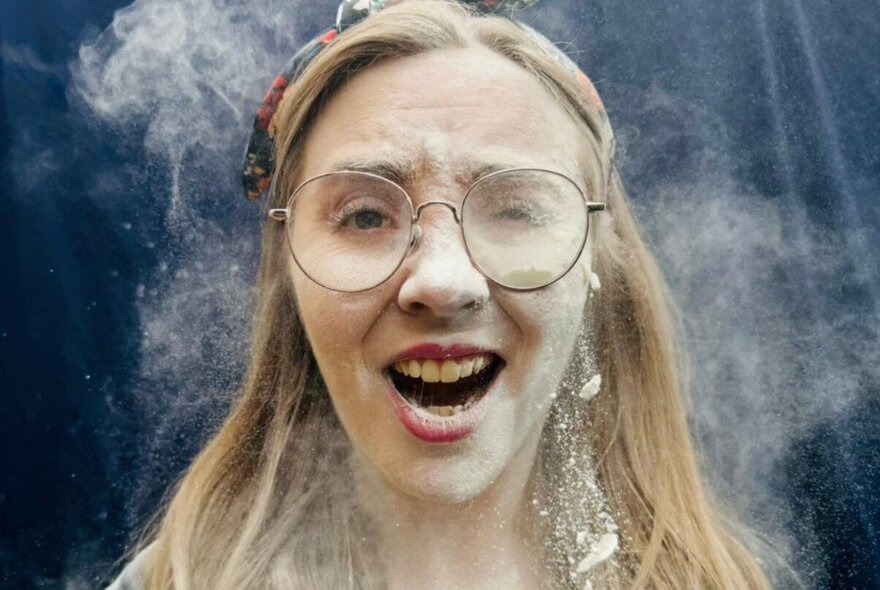 Comedian wearing round glasses in a haze of white powder.