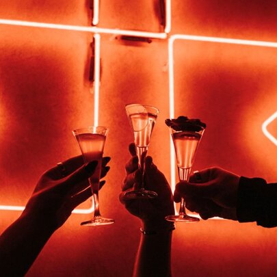 Three mini cocktails held against a neon sign.