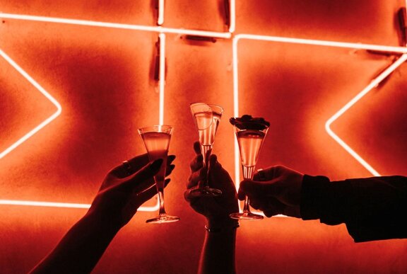 Three mini cocktails held against a neon sign.