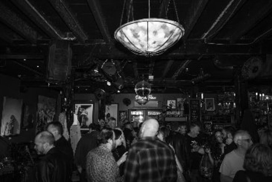 People in a crowded bar with mirror ball and suspended lighting.