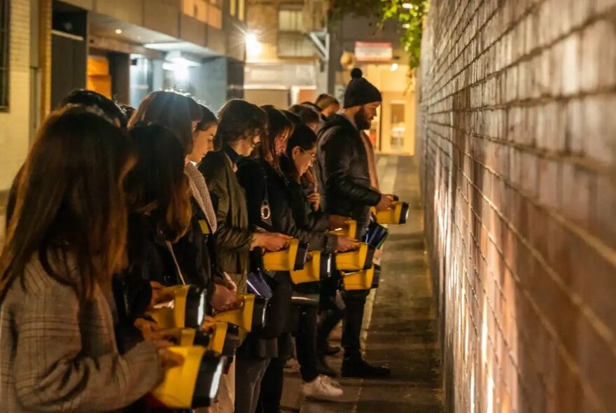 Walking tour group at night shining torches onto a brick wall.