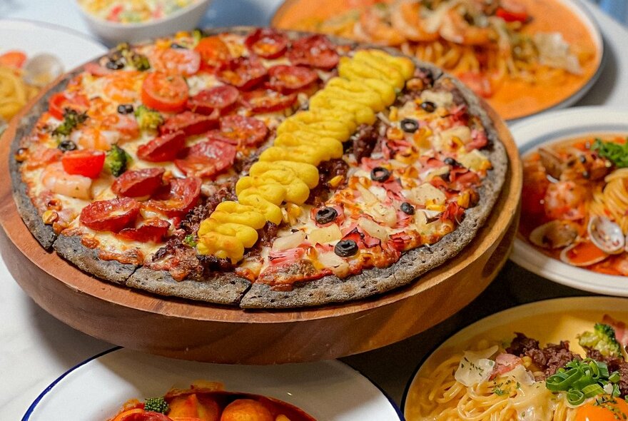 View of a table with many plates and a pizza in the centre with lines of toppings. 