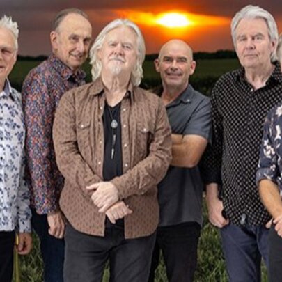 Country rock musicians wearing Western-style shirts, standing in a row with the sun setting behind them.