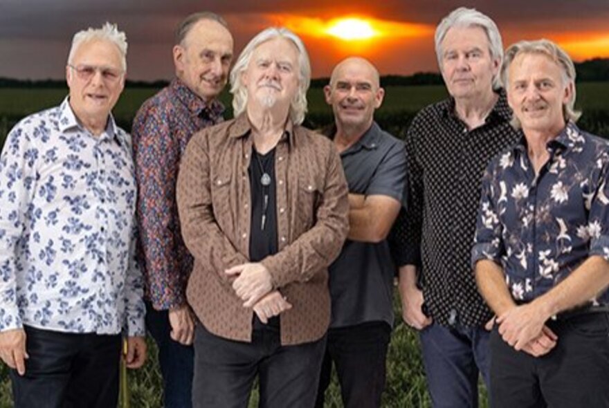Country rock musicians wearing Western-style shirts, standing in a row with the sun setting behind them.