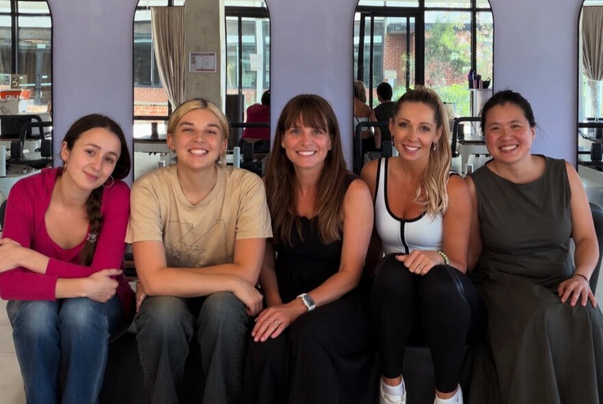 Five smiling women sitting down in a row and posing for a photo.
