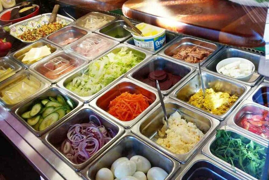 Different salad items chopped up and displayed in metal containers