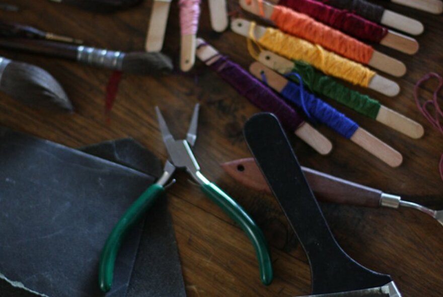 Sewing and craft tools and accessories, including rainbow coloured thread on spools, resting on a wooden table.