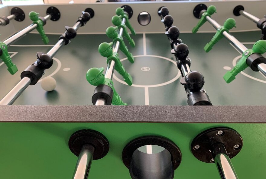 A close-up image of a foosball table with green and black players.