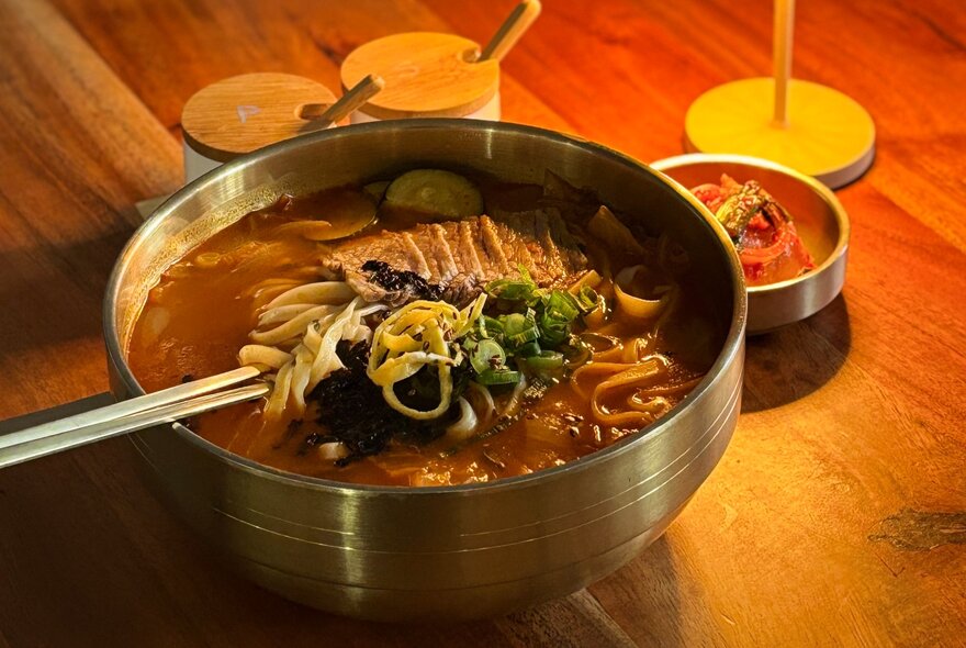 Looking down on a table with a Korean hotpot dish in the centre, chopsticks twirled around some noodles and condiments. 