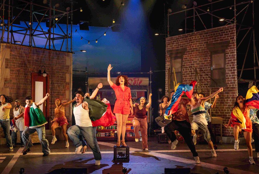 A cast of actors dancing and singing in a musical theatre production on a stage.