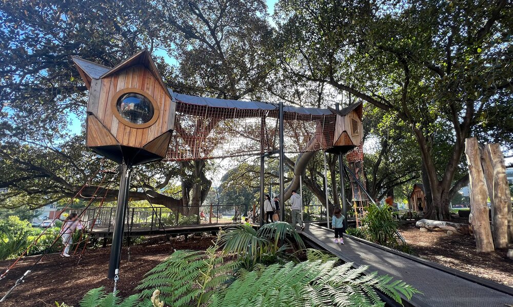 A timber playground with a lookout tower in a leafy park.