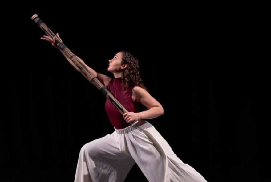 Performer holding a totem pole, stretching her arm and legs.