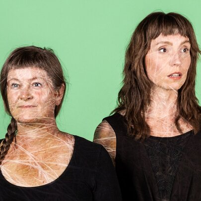 Two individuals wearing plain black tops with similar textured patterns on their skin, posed against a solid green background.