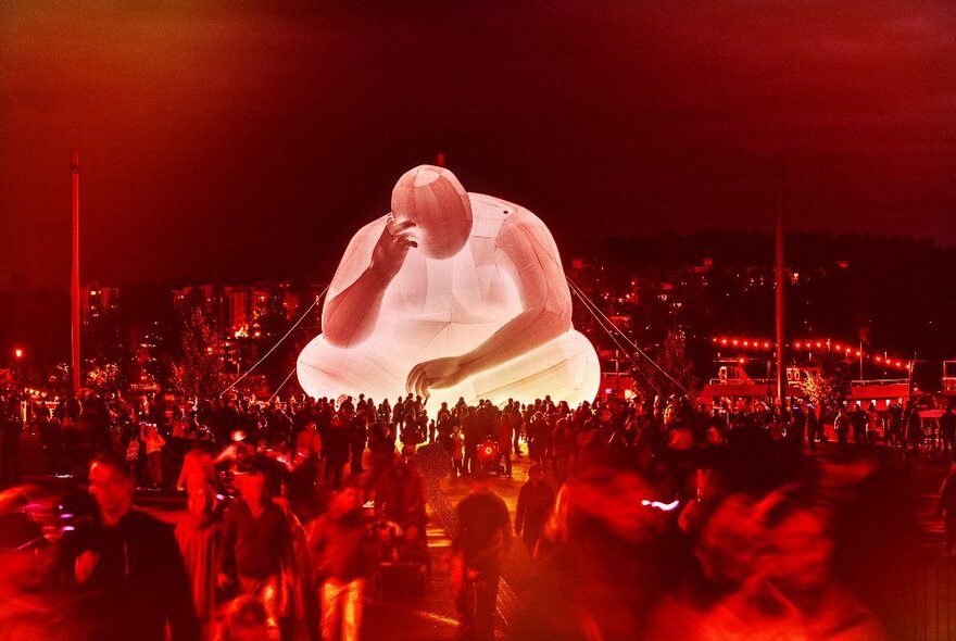 A large illuminated inflatable sculpture, with crowds walking around outdoors at night, at the Firelight Festival.