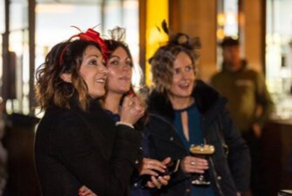 Three women wearing fascinators in a bar setting. 