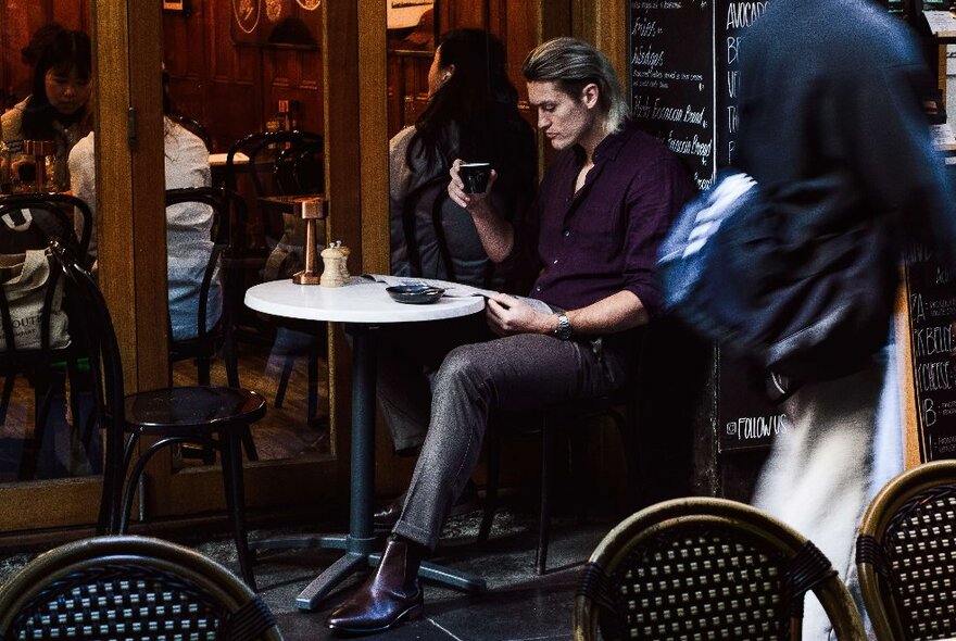 Darcy Moore sitting at a cafe with a coffee in his hand. 