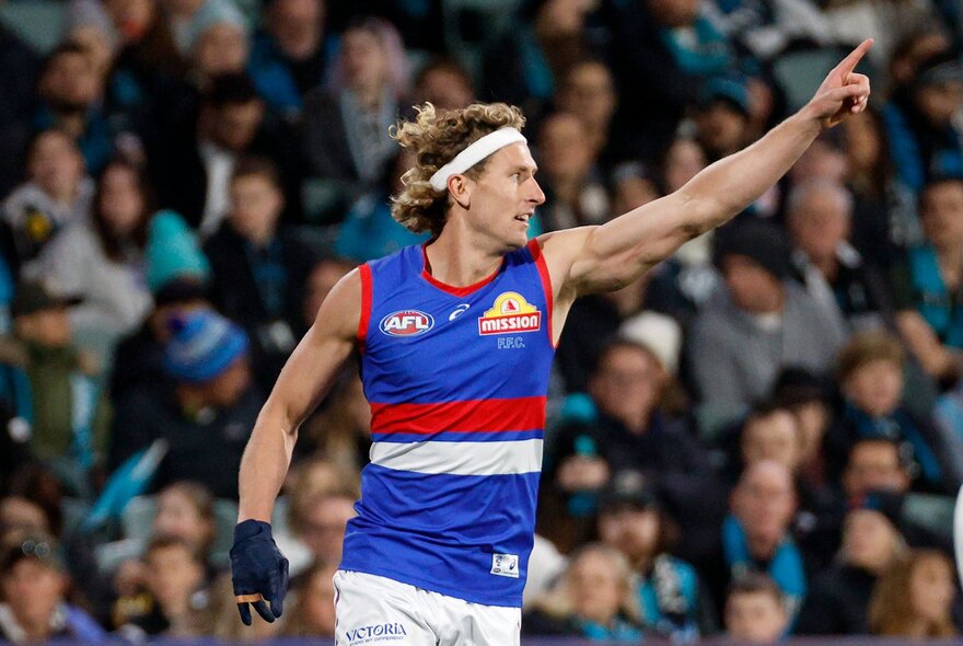 A Western Bulldogs AFL football player with his arm raised triumphantly, cheering himself and the fans along during a match.