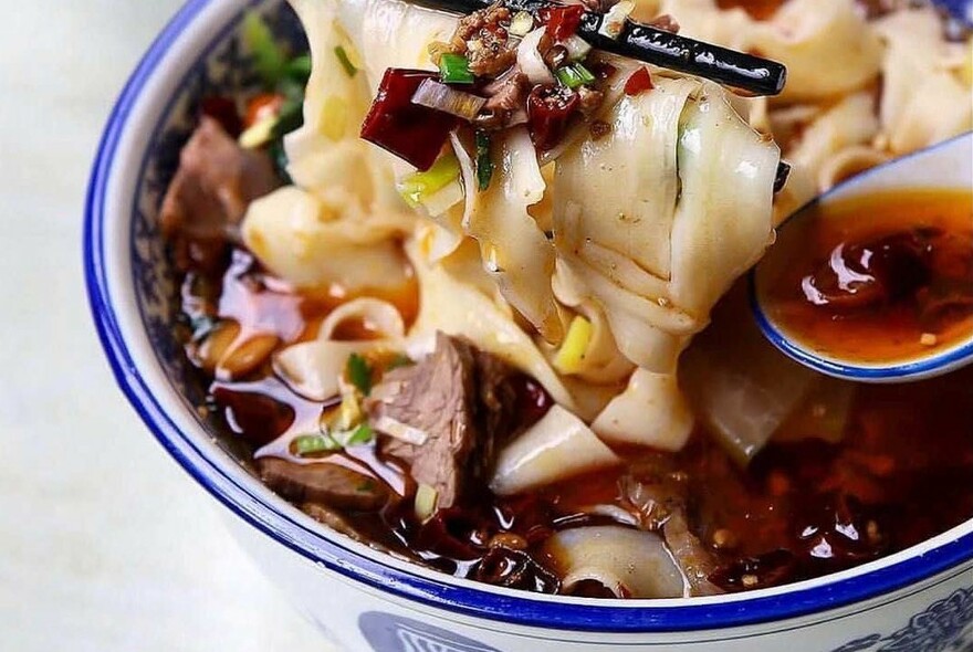 A spoon dipping into a bowl of soup with noodles.