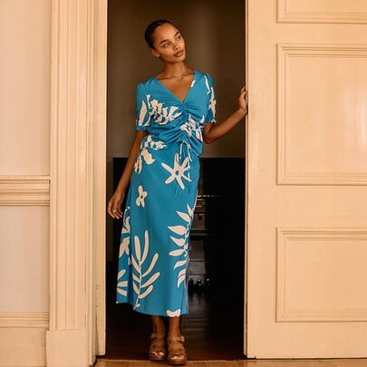 A model posing in a matching blue skirt and top with white leaf print.