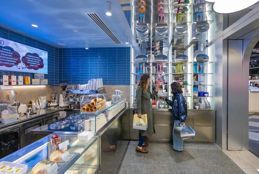 Two women with shopping bags in La Nuvola dessert bar, cakes on display.