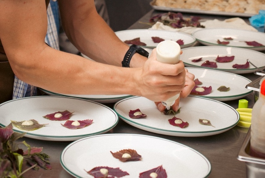 Plates lined up for service with a chef squeezing dots of sauce on top. 