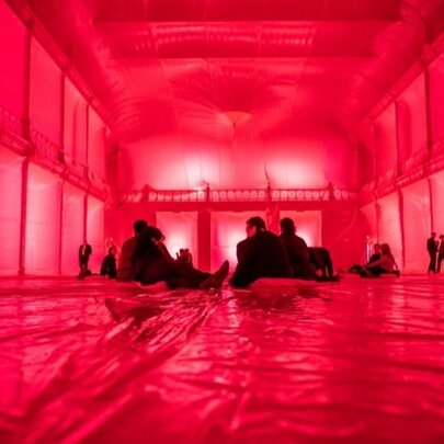 The red-lit interior of the Royal Exhibition Building, with people seated on the plastic-covered floor.