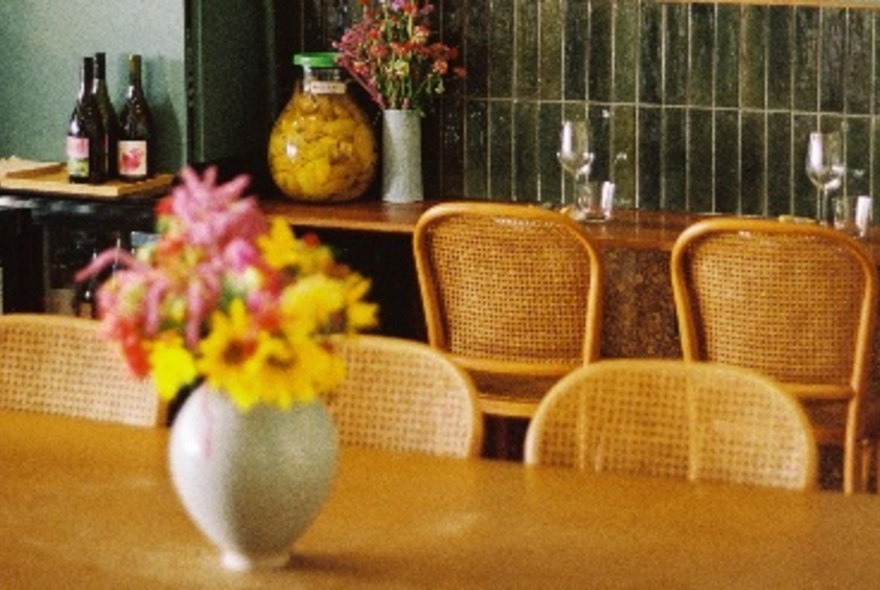 Restaurant table set with vases of flowers and preserved food, with bench table and stools.