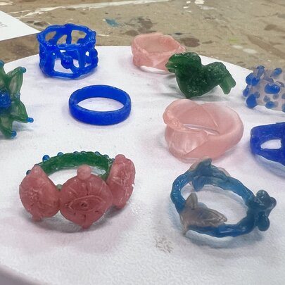 A collection of blue, pink and green rings made from jewellers' wax on a white marble surface.