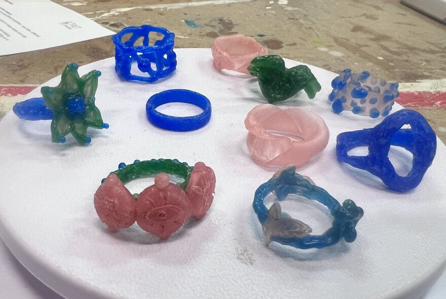 A collection of blue, pink and green rings made from jewellers' wax on a white marble surface.