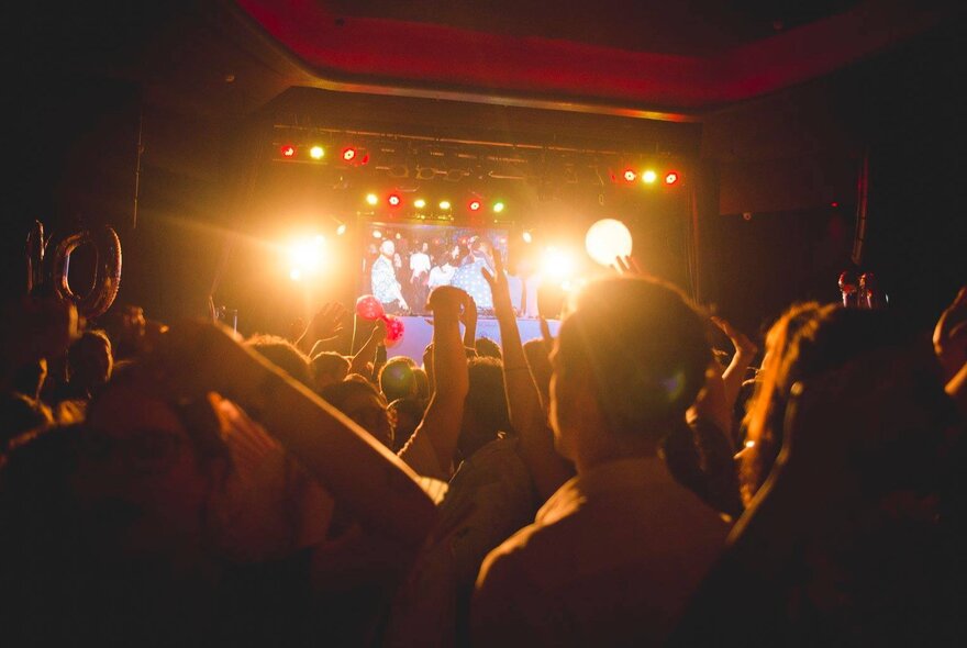 A nightclub scene with dancing people looking on at a brightly lit stage.