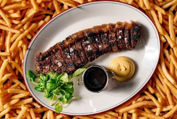 A Phoenix Wagyu rump steak on a plate with two sauces and a green garnish; surrounded by crunchy golden fries.