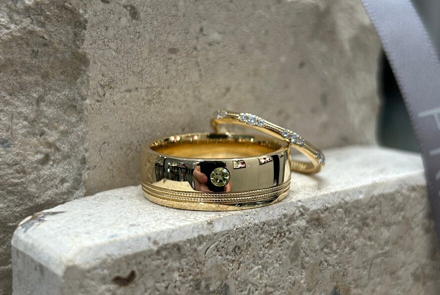 Two rings resting on each other, the bottom one is a wide gold ring with a central diamond inlay, the top ring is thinner.