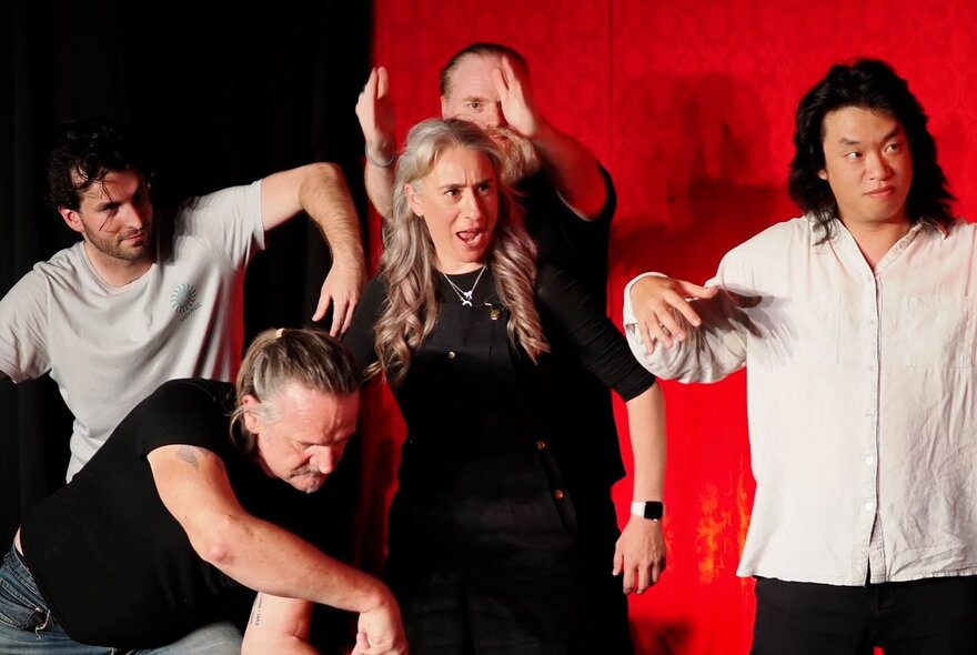 Five performers in close proximity improvising on a stage in front of a red curtain.