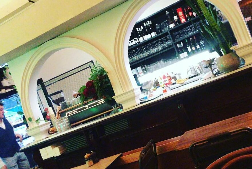 Interior of cafe showing bar and coffee service area with the tops of wooden tables visible in foreground.