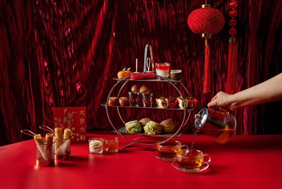 A three tiered high tea tray with spring rolls, tea and red lanterns.