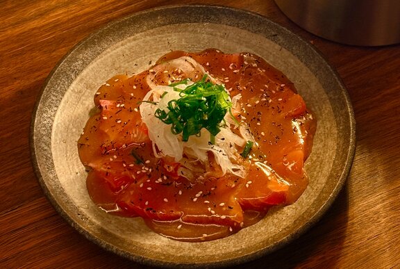 A round plate of salmon sashimi coated in a shiny sauce, with shredded daikon and greens as garnish.