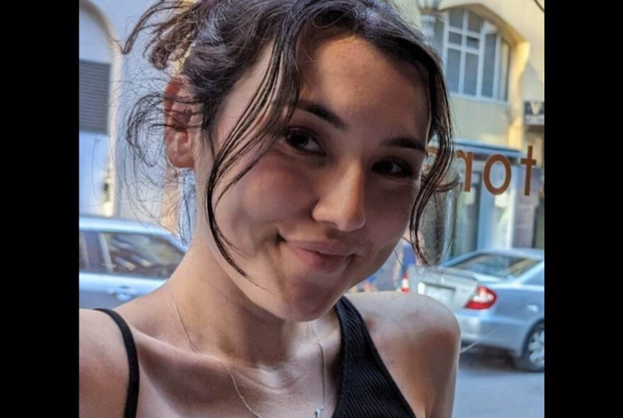 A candid image of a young woman smiling at the camera, with a building behind her.