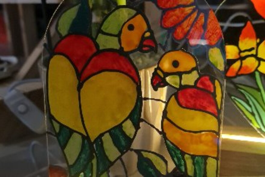 A close up of a painted glass lamp with parrots on it. 