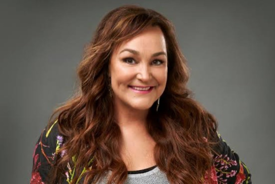 Media personality Kate Langbroek, with long brown hair, smiling at the viewer.