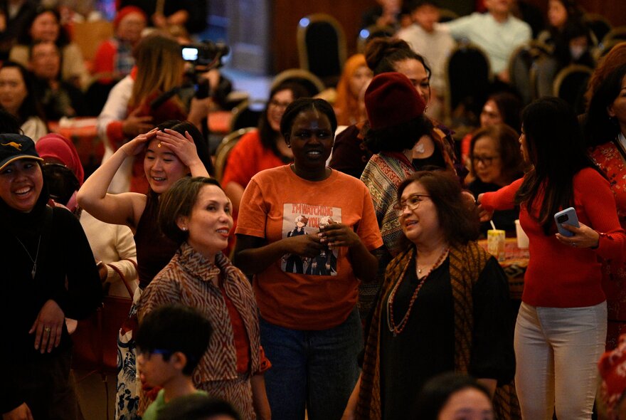 People standing chatting in a group, surrounded by seated people.