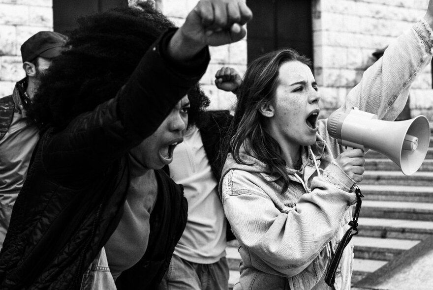 Demonstrators with megaphones, raising arms and shouting.