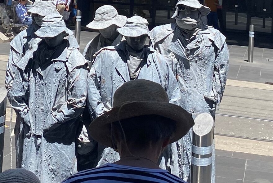 Five street performers dressed as grey statues the the back of a person looking on. 