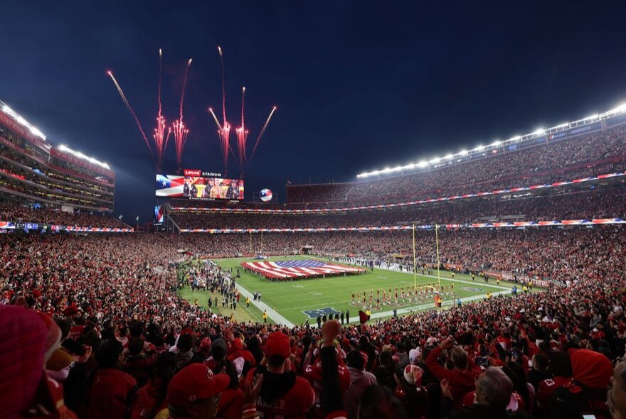 Huge sports stadium filled with fans as fireworks explode over a huge screen.