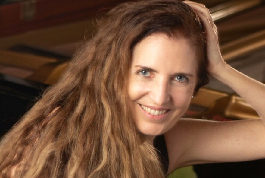 Portrait of internationally renowned pianist, Elyane Lausade, leaning against a piano with her flowing hair over her shoulder.