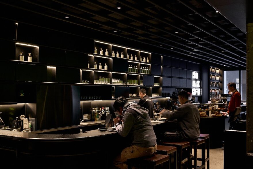 Dimly lit cafe interior with peole seated at the bar counter, tables and sofas in the background.