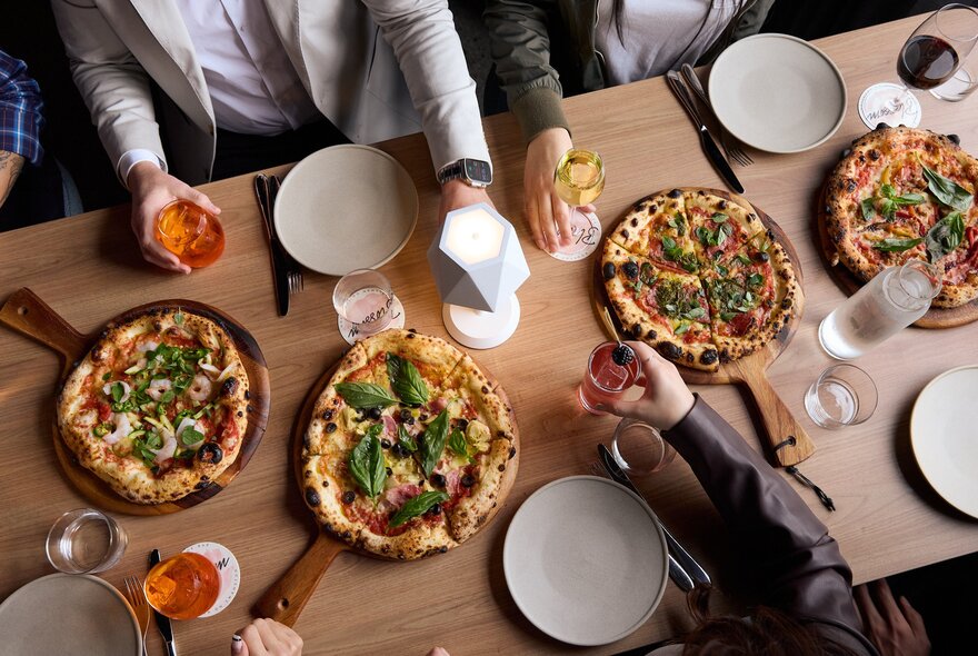 Looking down on a table at diners and four woodfired pizzas.