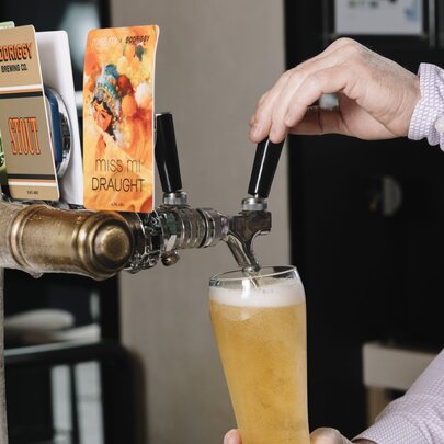 A hand using a beer tap to fill a pint glass with beer from behind a bar.